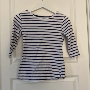 Randig tröja från Hampton Republic - Snygg vit och marinblå randig tröja från Hampton Republic med trekvartsärm och rund hals. Tröjan har ett broderat märke på ärmen med seglingsinspirerat motiv. Perfekt för en chill och stilren look.