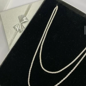Tunn silverfärgad kedja halsband - Stilrent halsband med tunn, glittrig kedja i silverfärg. Kedjan har en diskret och elegant design som passar perfekt till lager-på-lager eller för en minimalistisk look. Levereras i en snygg ask med silverrosett. 