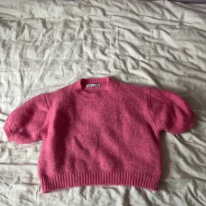 Rosa stickad tröja från Zara - Superfin rosa stickad tröja från Zara med korta puffärmar och ribbade muddar. Tröjan har en rund halsringning och är croppad i modellen, perfekt för att ge en trendig vibe till din outfit.