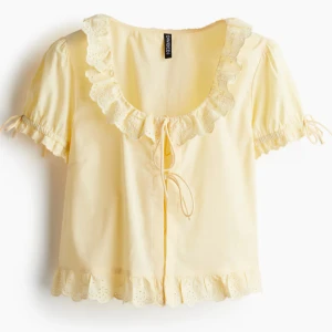 Gul blus med volang - Supersöt ljusgul blus från Divided med broderade volanger vid halsringning och nederkant. Korta puffärmar med knyt och volangdetaljer. Nyskick. 🌸✨🌻