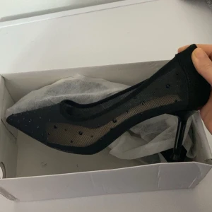 Svarta pumps med spetsig tå - Eleganta svarta pumps med spetsig tå och klack. Skorna har ett transparent mesh-material dekorerat med små svarta pärlor för en glittrig effekt. Perfekta för en stilfull look. Nya och oanvända då de var fel storlek!