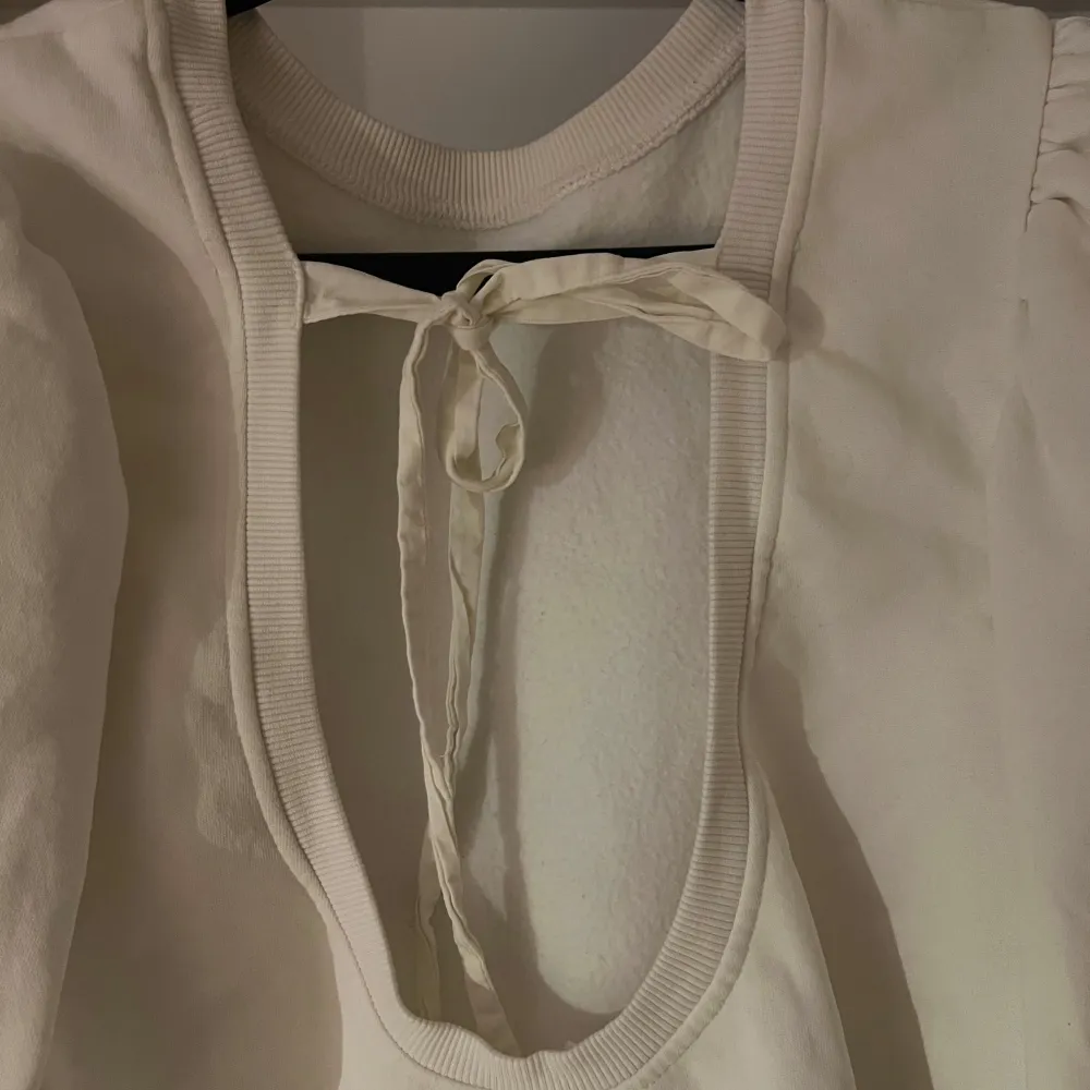 Säljer en stilren vit tröja med långa ärmar och en  öppen rygg med knytband från H&M. Tröjan har en rund halsringning och puffiga ärmar som ger en trendig touch. Storlek M. Neuletakit & Villapaidat.
