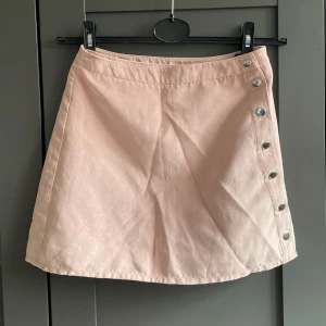 Rosa kjol i mocka-imitation - Ljusrosa kjol med knappar längs sidan som går att knäppa upp helt.