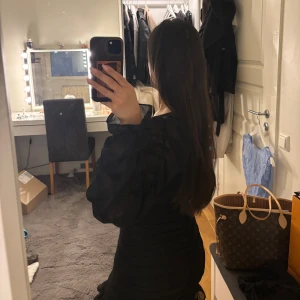 Svart klänning med volangdetaljer - Snygg svart klänning med v-ringning och långa ärmar. Från nakd strl 32, passar 34 också. Deffekt vid höften, har sytt. 