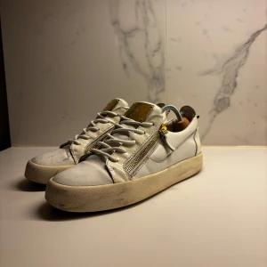 Guiseppi Zanotti Skor - Snygga vita sneakers med gulddetaljer och dragkedja på sidan. Skorna har en rund tå och snörning framtill. Perfekta för en stilren look. Skorna tvättas och färgkorrigeras innan frakt!✅