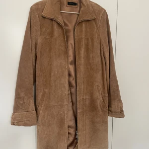 Brun mockajacka från Estelle - Säljer en snygg brun mockajacka från Estelle med dragkedja framtill. Jackan har långa ärmar och en klassisk krage. Perfekt för höst och vår!