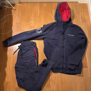 Mörkblå hoodie och byxor från Race Marine - Säljer en mörkblå hoodie med dragkedja och matchande byxor från Race Marine. Ny pris 1000krHoodien har en röd insida i huvan och broderad text på ärmen. Byxorna har snörning i midjan och röda detaljer vid fickorna. Priset kan alltid diskuteras!.