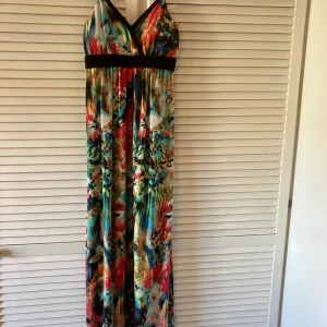 Färgglad långklänning från Stella Morgan - Säljer en färgglad långklänning från Stella Morgan med ett abstrakt mönster i flera färger. Klänningen har en v-ringad design och smala axelband. Den har en svart flätad detalj under bysten som ger en fin kontrast.