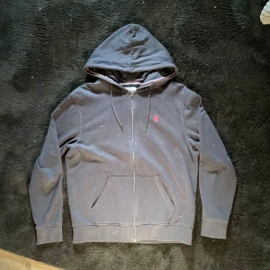 Polo Zip Hoodie - Säljer nu min mörkblåa zip från U.S. Polo Assn. med en klassisk röd logga på bröstet. Tröjan är väldigt stilren och skicket ut med strecken i luvan. Perfekt till varmare tider!