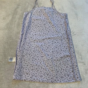 Ljusblå ärmlös klänning med blommigt mönster - Söt ljusblå klänning med små blommor i ett mörkare mönster. Klänningen är ärmlös med smala axelband och har en rak passform. Perfekt för varma dagar!