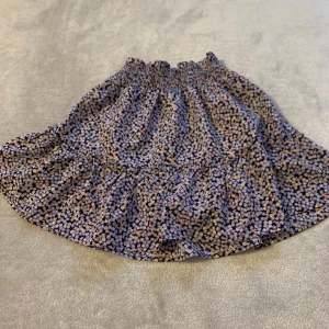 Blommig kortkjol med volang - Charmig kortkjol med blommigt mönster i blått och rosa. Kjolen har en volangdetalj och elastisk midja för en bekväm passform. Perfekt för en somrig look!