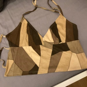 Patchwork korsettopp från Lovelection - Säljer en unik patchwork korsettopp från Lovelection i olika nyanser av brunt och beige. Toppen har justerbara axelband och en snygg design med triangulära mönster. Perfekt för att ge en bohemisk touch till din outfit. Aldrig använd, helt ny! Pris:350kr