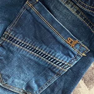 Blå jeans med resår och slitningar - Snygga blå jeans med resår i midjan och vid bensluten. De har coola slitningar på framsidan och en praktisk snörning i midjan. Perfekta för en avslappnad stil.