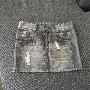 Grå jeanskjol från Ginatricot - Snygg grå jeanskjol från Ginatricot med slitna detaljer och klassisk femficksdesign. Perfekt för en avslappnad look. Kjolen har en knapp och dragkedja framtill.