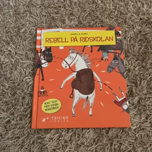 Rebell på Ridskolan - Boken 'Rebell på Ridskolan' av Camilla Kuhn är en färgglad barnbok med kort text och stora bokstäver, perfekt för unga läsare. Den handlar om hästen Rebell som går på ridskola. Omslaget är orange med illustrationer av hästar och en humoristisk stil. Den är från McDonald’s 2018!