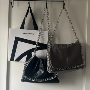 Axelväskor från Tiamo - Två snygga axelväskor från Tiamo med kedjedetaljer. En i svart och en i grå/beige. I jättefint skick, man kan ha kedjan kort och lång🫶🏻200 för en