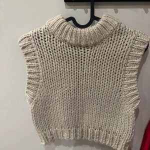 Beige stickad väst - Säljer en mysig beige stickad väst med ribbad krage och nederkant. Perfekt för lager-på-lager under kyligare dagar. Enkel och stilren design som passar till det mesta.
