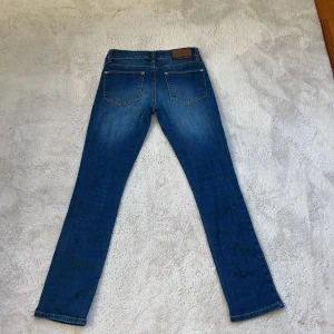 Blå jeansbyxor - Snygga blå skinny jeansbyxor från Lager 157 med klassisk femficksdesign och knappgylf. Perfekta för en avslappnad stil. Märkeslappen i brunt läder är lite sliten dock. Ena fickan finns en fläck men syns ej så mycket. Storlek 150.