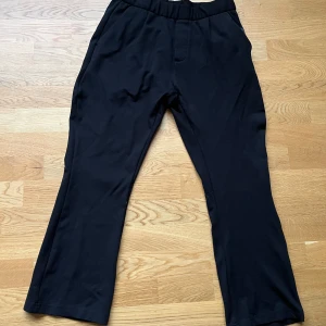 Svarta kostymbyxor från Lager 157 - Svarta kostymbyxor från Lager 157 med elastisk midja och raka ben. Byxorna har diskreta fickor bak och är tillverkade i ett mjukt, stretchigt material som känns bekvämt hela dagen. 