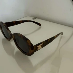 Bruna ovala solglasögon från Celine - Snygga solglasögon från Celine med oval form och sköldpaddsmönstrad båge i bruna och svarta toner. Sidorna har den ikoniska Celine-loggan i guld.