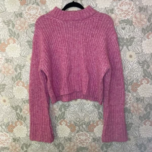 Rosa stickad tröja från Gina Tricot - Mysig rosa stickad tröja från Gina Tricot med hög krage och breda muddar. Tröjan har en loose passform och är perfekt för kyliga dagar. Ribbstickad struktur och något croppad längd ger en trendig vibe.