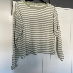 Randig långärmad tröja från Monki - Grön och vit randig långärmad tröja från Monki i mjuk bomull. Tröjan har en relaxed fit med rund halsringning och klassiska horisontella ränder. Perfekt för en chill och avslappnad stil. OBS liten lagning på ärmen, syns inte men viktig detalj.