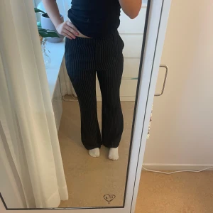 Svarta randiga kostymbyxor NA-KD - Snygga svarta kostymbyxor från NA-KD med vita tunna ränder. Byxorna har hög midja och bootcut. Materialet är väldigt mjukt.