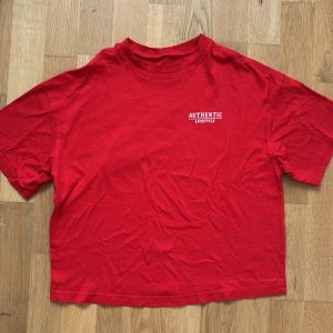 Röd XS t-shirt Authentic Lifestyle från H&M  - Röd t-shirt med vit tryckt text 'AUTHENTIC LIFESTYLE' på bröstet från H&M. Oversized passform med korta ärmar och rund halsringning. Skön och mjuk i bomull, perfekt för en chill och avslappnad look. Size XS. 