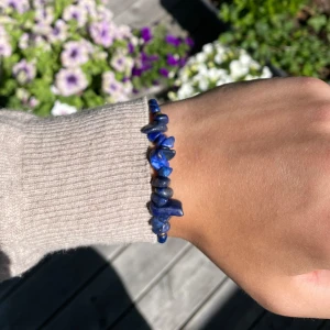 Blått armband med stenar och gulddetaljer  - Snyggt armband med blå stenar och små runda pärlor i mörkblått och guld. Justerbar knytning för perfekt passform. Perfekt accessoar för att ge din outfit lite extra färg och stil.