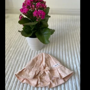 Ljusrosa solhatt från Newbie, barn 4-9 månader  - Supersöt ljusrosa solhatt från Newbie i mjuk bomull. Hatten har bred brätte och fina knytband i spets framtill. Perfekt för soliga dagar och ger en gullig vintagekänsla till outfiten.