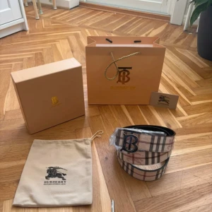 Burberry rutigt skärp med BB-spänne Guld - Snyggt Burberry-bälte i klassiskt rutig design med beige, bruna och svarta toner. Bältet har ett stort metallspänne med BB-logga och är gjort i exklusivt skinn. Perfekt accessoar för att lyfta din outfit med en lyxig touch.