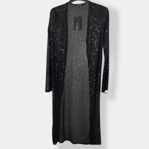 Svart paljett kofta Fashion Nova - Lång svart cardigan kofta från Fashion Nova, täckt med glittriga paljetter som ger en riktigt snygg och festlig look. Koftan är öppen framtill, har lång ärm och är tillverkad i ett lätt, stickat material. Perfekt för att lyfta vilken outfit som helst.