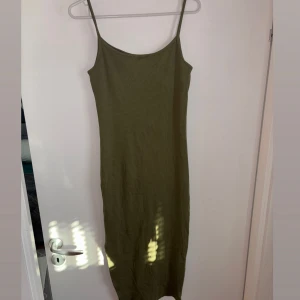 Olivgrön långklänning med smala axelband och slits - Säljer en olivgrön långklänning med smala axelband och rak passform. Klänningen är ärmlös och har en enkel, stilren design som passar perfekt till varma dagar. Materialet känns mjukt och lätt mot huden.