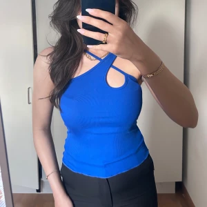 Kornblå ribbad linne från SHEIN - Säljer en kornblå ribbad linne från SHEIN i storlek S. Toppen har en unik asymmetrisk design med smala axelband som korsas och en cut-out detalj vid axeln. Materialet är stretchigt och sitter tight mot kroppen. Perfekt för dig som gillar trendiga och snygga toppar!