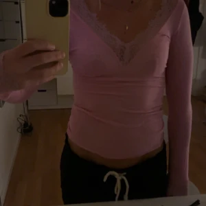Rosa intimissimi tröja - Säljer en söt rosa långärmad topp med v-ringning och spetsdetaljer längs halsringningen. Toppen är figurnära och har en feminin look som passar perfekt till jeans eller kjol. Superfin färg och mjukt material!