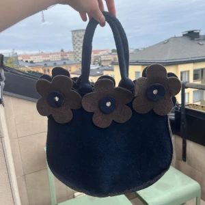 Blå handväska med blommor - Unik handväska i mörkblå filt med stora bruna  blommor längs kanten.  Säljer pga ÖVERFLÖD av handväskor. Perfekt för dig som vill sticka ut med din stil. Kramis❤️❤️