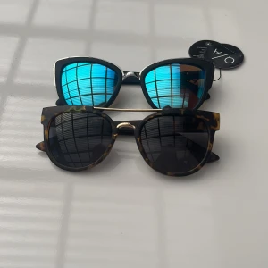 Två trendiga solglasögon från Quay Australia - Säljer två par solglasögon från Quay Australia. Ena paret har spegelblå kattögonformade linser med svarta bågar kallas MY GIRL, det andra har klassisk brunmelerad båge med svarta linser och gulddetalj upptill. Perfekta accessoarer för att lyfta din stil kallas ODIN