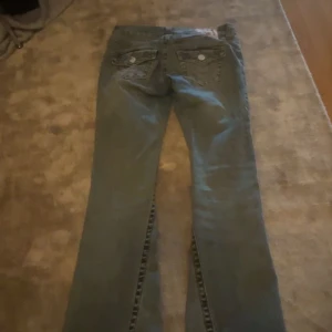 True Religion bootcut jeans blå - Snygga blå jeans från True Religion med klassiska broderade bakfickor och knappar. Modellen har bootcut-ben och normal passform. Jeansen är i denim med ljus tvätt och har detaljerade sömmar på fickorna. ( pris 950kr går att diskutera)
