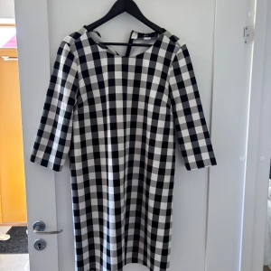 Rutig klänning från Ellos, svart/vit - Snygg rutig klänning från Ellos i svart och vitt. Modellen är rak med trekvartsärm och rund halsringning. Klänningen har dragkedja bak