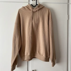Beige oversized hoodie med huva - Säljer en oanvänd, enkel och stilren beige hoodie med huva och dragsnören. Oversized passform med långa ärmar och breda muddar vid ärmslut och nederkant. Mjuk bomullskänsla, perfekt för chill dagar eller när du vill ha en avslappnad look.