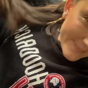 Svart hoodie med tryck från Hoodrich - Svart hoodie från Hoodrich med stort vitt tryck över bröstet och ett runt märke i rött, vitt och blått. Klassisk huva och sportig vibe, perfekt för dig som gillar streetwear. Snygg och bekväm att bära till jeans eller joggers. Hör av er om intresse hela settet kan diskuteras men säljer hyfsat dyrt för att detta inte går att köpas längre💓