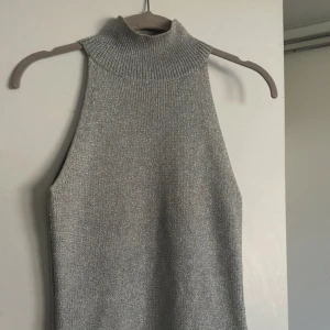 Halterneck topp - Snygg grå stickad polotopp med hög krage och ärmlös design. Perfekt för lager-på-lager eller att bära som den är. Tidlös och enkel att matcha med olika stilar.
