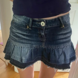  jeanskjol med volang - Supersöt  jeanskjol från Kookai med volangkant och fransig nederdel. Kjolen har klassiska jeansfickor fram och bak, bälteshällor och en snygg knapp framtill. Perfekt för dig som gillar en cool och avslappnad stil. Storlek s. 