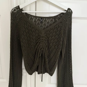 Olivgrön stickad tröja från Only - Supersnygg olivgrön stickad tröja från Only med v-ringning och lång ärm. Tröjan har ett genomgående hålmönster och cool snörning framtill som ger en croppad känsla. Perfekt att styla med jeans eller kjol för en trendig look. Helt oanvänd så är i perfekt skick!