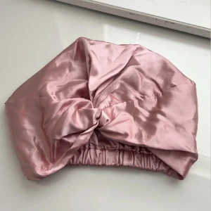 Rosa satin turban med knut - Snygg turban i glansig rosa satin med en stor knut framtill. Mjuk resår baktill för skön passform. Perfekt accessoar för att lyfta din look med en touch av lyxig vibe. Passar dig som gillar trendiga och bekväma huvudbonader. Oanvänd!