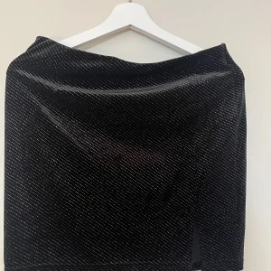 Svart glittrig kortkjol FB Sister - Svart kortkjol från FB Sister med glittriga prickar över hela tyget. Kjolen har en liten slits framtill som ger en snygg detalj. Perfekt för dig som vill sticka ut lite extra med en cool och trendig look.