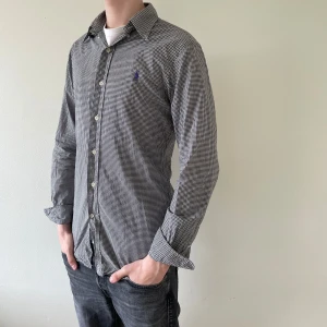 Polo Ralph Lauren Skjorta - Sjukt snygg Polo Ralph Lauren skjorta i en vit & svart rutig färg med lila logga. Skjortan är i slimfit passform och är i storlek S. Modellen är runt 184cm. Pris kan diskuteras, hör av dig vid funderingar!🤩