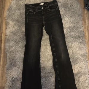 Svarta jeans från Gina Tricot, stl 158 - Svarta jeans från Gina Tricot med snygga kontrastsömmar och klassisk femficksdesign. Jeansen har raka ben och silverfärgade knappar och nitar. Perfekta för dig som gillar en stilren look med lite edge.