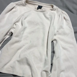 Vit långärmad topp från Vero Moda - Säljer en stilren vit långärmad topp från Vero Moda. Modellen har lätt puffade axlar och rund halsringning. Tillverkad i mjuk bomullsmix som känns skön mot huden. Perfekt för dig som gillar en enkel men trendig look.