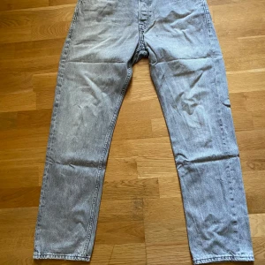 Grå jeans från Jack & Jones - Säljer ett par grå jeans från Jack & Jones med klassisk femficksdesign och snygga bakfickor med broderad detalj. Jeansen har normal passform och raka ben, tillverkade i bomull med en ljusgrå tvätt. Perfekta för en avslappnad och stilren look.